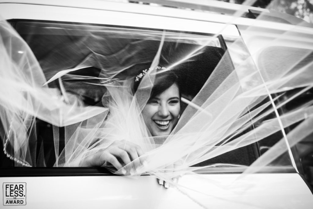fearless award wedding photos Novia sonriente en auto y envuelta en su velo. Foto en blanco y negro