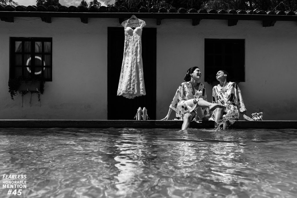 fearless award wedding photos. Novia sonriente junto a su hermana con piesa en la piscina y el vestido colgado. Foto en blanco y negro