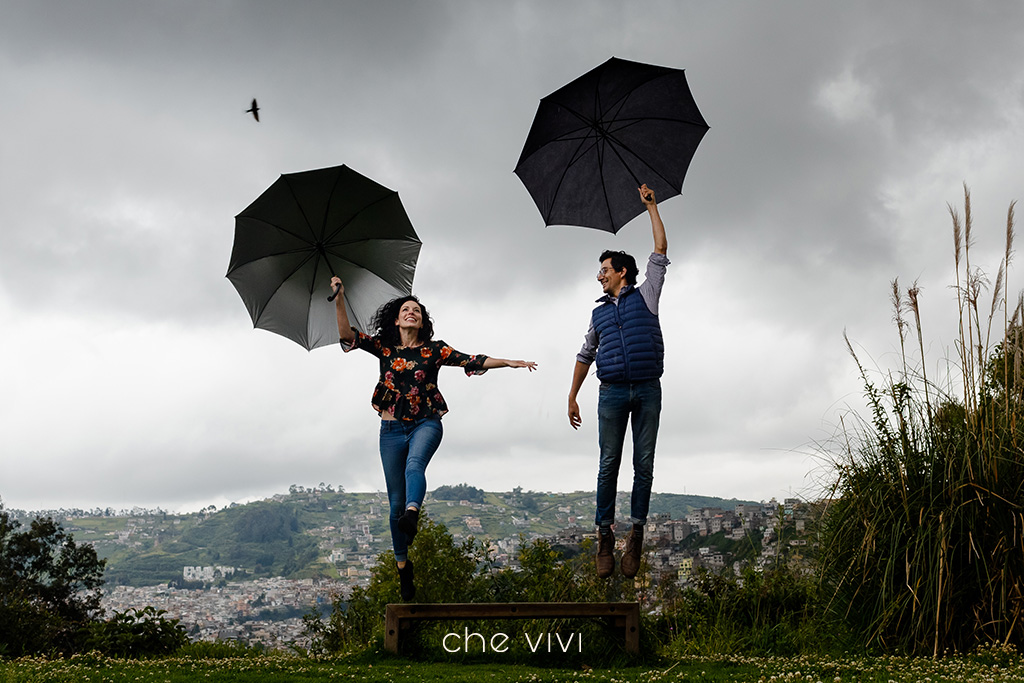 Couple jumping off a bench holding black umbrellas