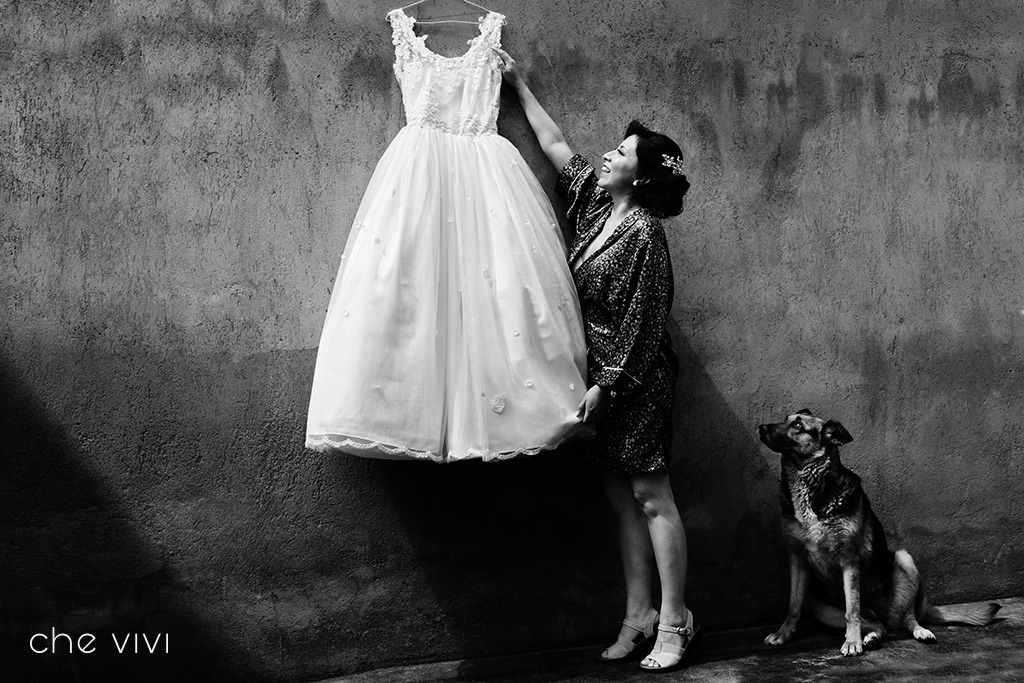 Novia cuelga su vestido de novia mientras su perro pastor alemán la observa. Bodas con mascotas.
