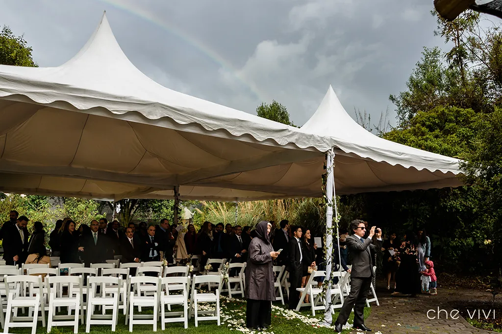 Invitados esperando la entrada de la novia en carpas con arco iris en el cielo boda Quito.