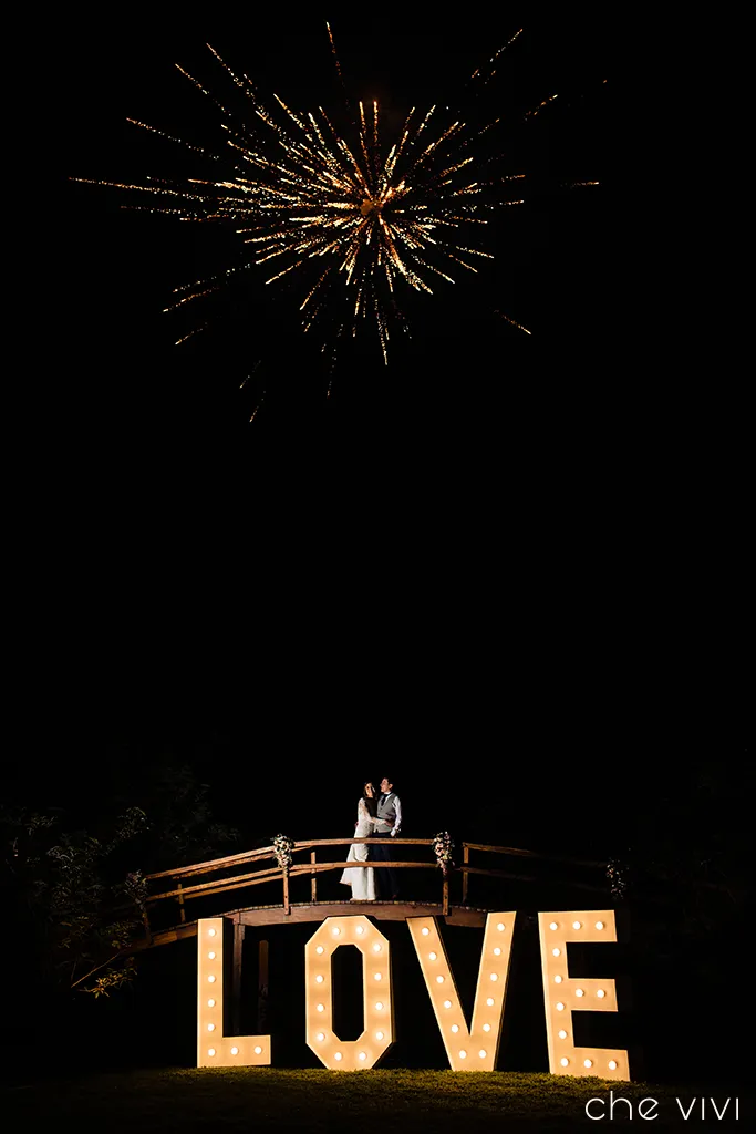 Letras Love con novios en puente y fuegos artificiales a la noche en lugar para boda La Lomita Quito.