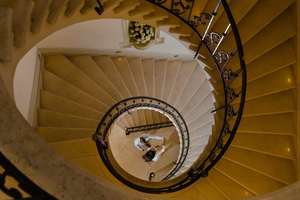 Toma cenital de una pareja bailando en la elegante escalera de caracol del Hotel Casa Gangotena. Una perspectiva artística y diferente de tu compromiso en Quito.