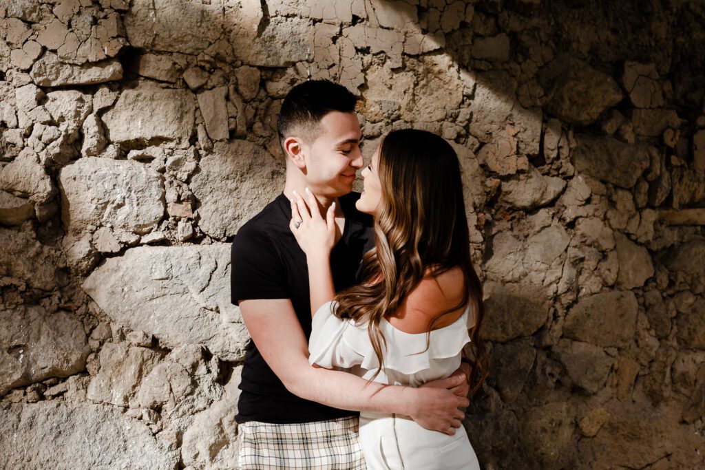 Captura cercana de una pareja compartiendo una mirada cómplice frente a un muro de piedra antiguo. Fotografía documental de bodas y parejas en Quito por Viviana.