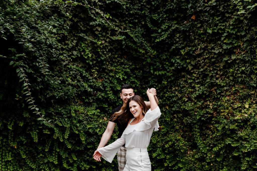 Pareja bailando y riendo frente a una pared de hiedra natural en el Parque de Guápulo. En Che Vivi priorizamos que disfrutés el momento mientras nosotros capturamos la magia.